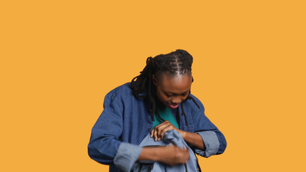 Joyous woman rummaging through backpack for school notebooks, studio background