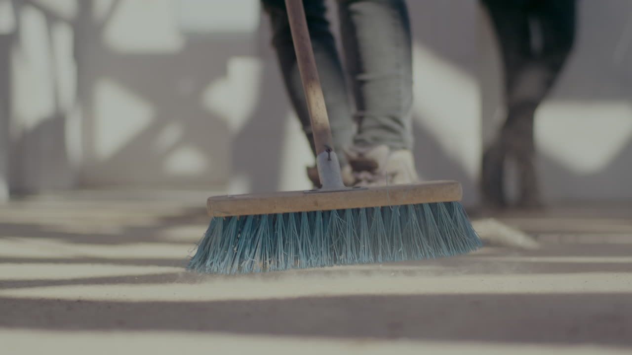 Low section of female worker sweeping floor with broom at construction site