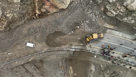 Drone-tilting-up-movement-aerial-shot-of-yellow-bulldozer-clearing-the-landslide