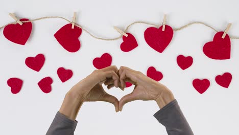 Concepto-Del-Día-De-San-Valentín-Con-Manos-Haciendo-Forma-De-Corazón-Contra-Fondo-Blanco-Con-Corazones-Rojos-Atados-A-Una-Cuerda