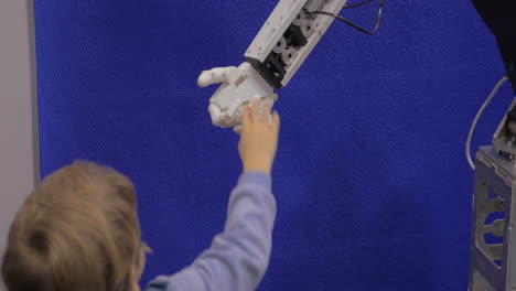 close up view of boy hand holds white moving plastic hand of humanoid robot in robotics exhibition in moscow russia