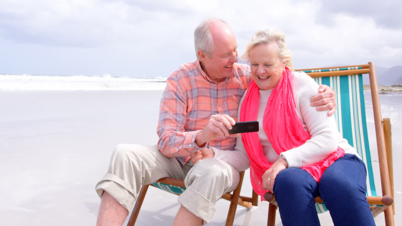 휴대 전화 를 사용 하고 해변 에 앉아 있는  ⁇ 은 백인 노인 부부 의 앞 면 4k