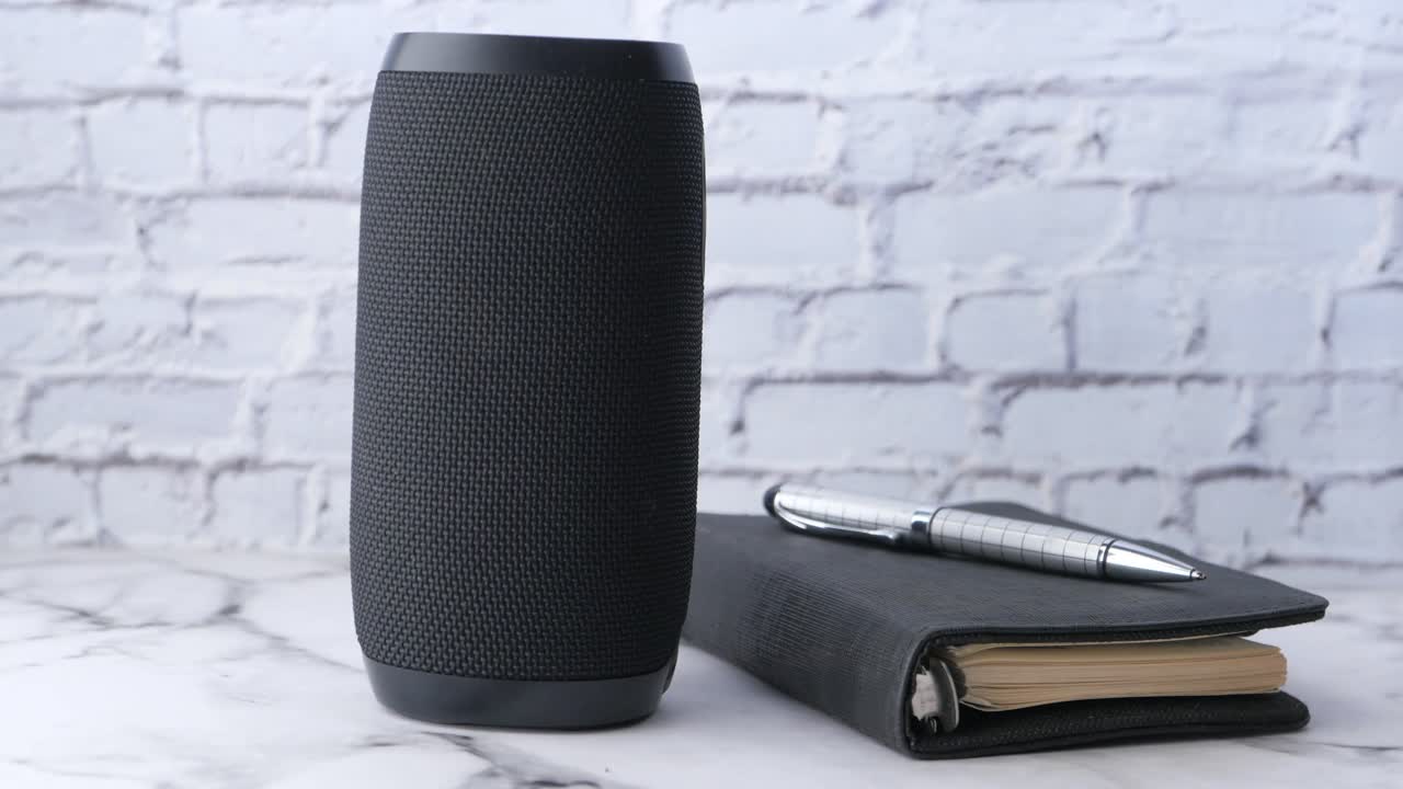 altavoz portátil, cuaderno y bolígrafo en un escritorio de mármol