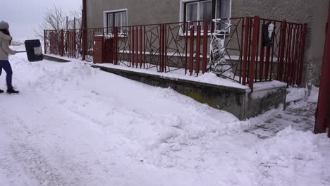 joven mujer de moda en ropa de invierno paleando nieve fuera de casa