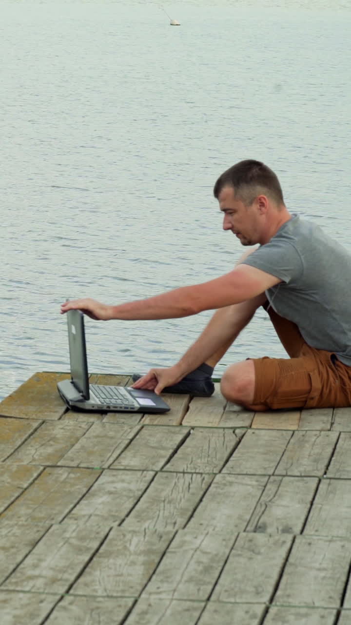 Man on the pier working on a laptop. Vertical video