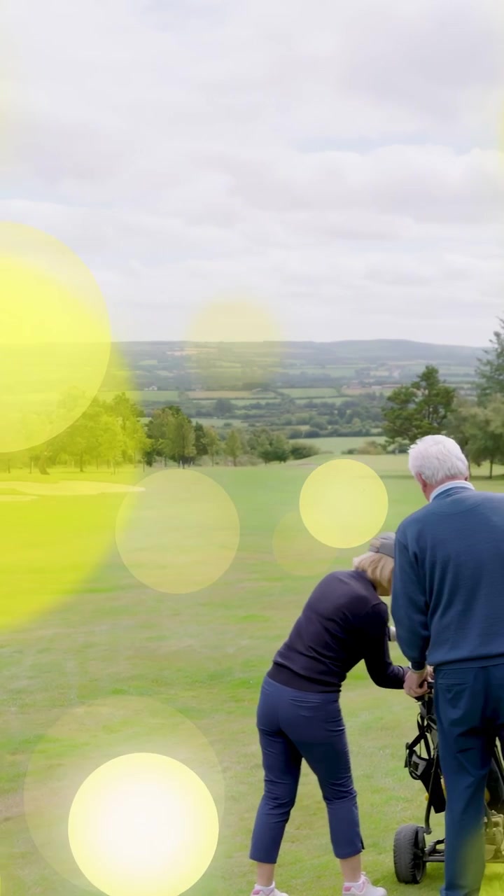Vertical video: Seniors leaving trees golfing pushing trolley adjusting to bunker with yellow bokeh