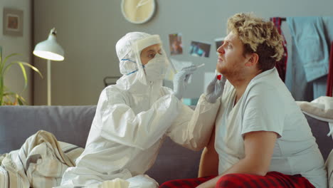 doctor in protective suit testing patient for covid-19 at home