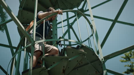 man walkig upstairs on a spiral stairway with an orange backpack to reach top of a lookout tower