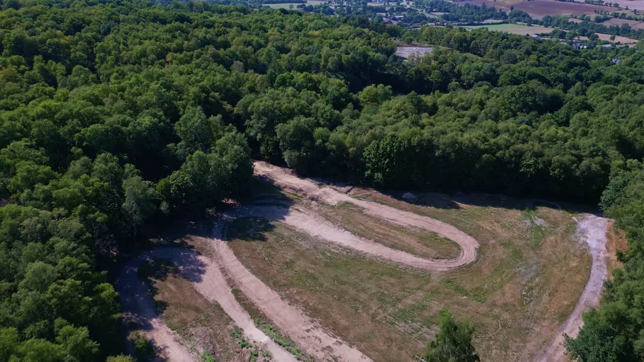 Forward drone movement over a dirt road cutting through dense green forest landscape in summer, Mayenne, France