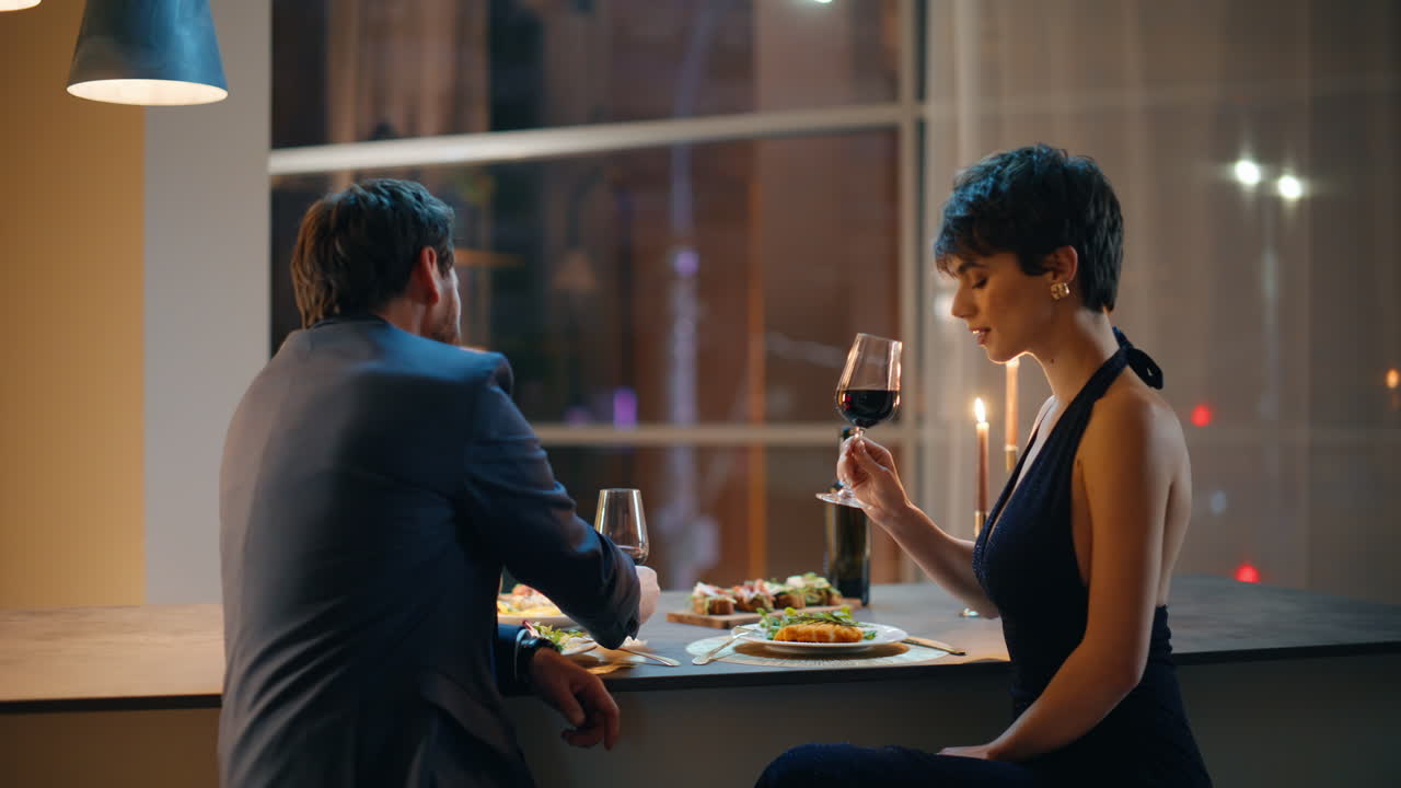 Amanti sorridenti che brindano con calici di vino, trascorrendo una serata romantica seduti al bancone del bar