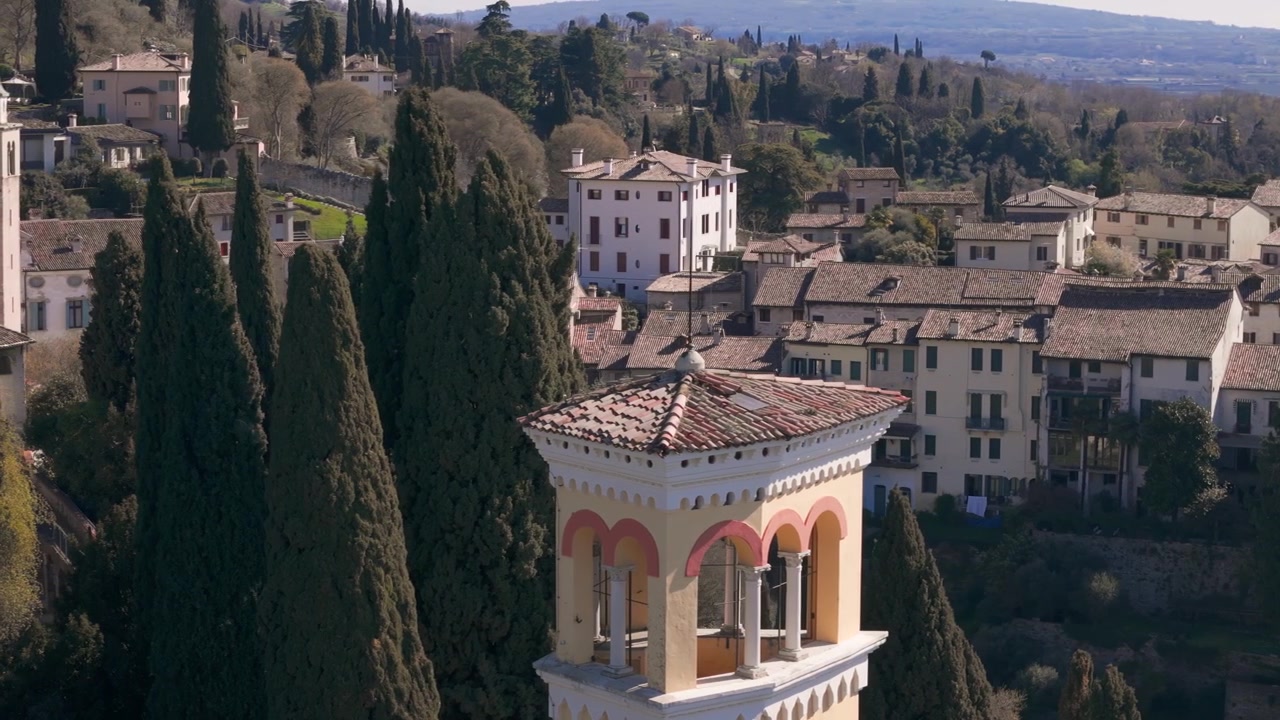 Il campanile si erge sopra i cipressi e gli edifici storici nella soleggiata Asolo, Italia