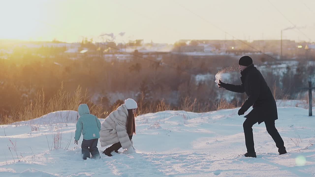 padre madre hijo en ropa de invierno arroja nieve seca al atardecer