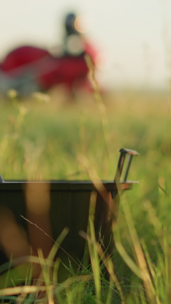 검은색 바구니와 수건이 잔디의 전면에서 보이며, 모터사이클이 배경에 흐릿해지면서 두 사람이 나타났고 열린 에서 바구니를 들고 갔다.