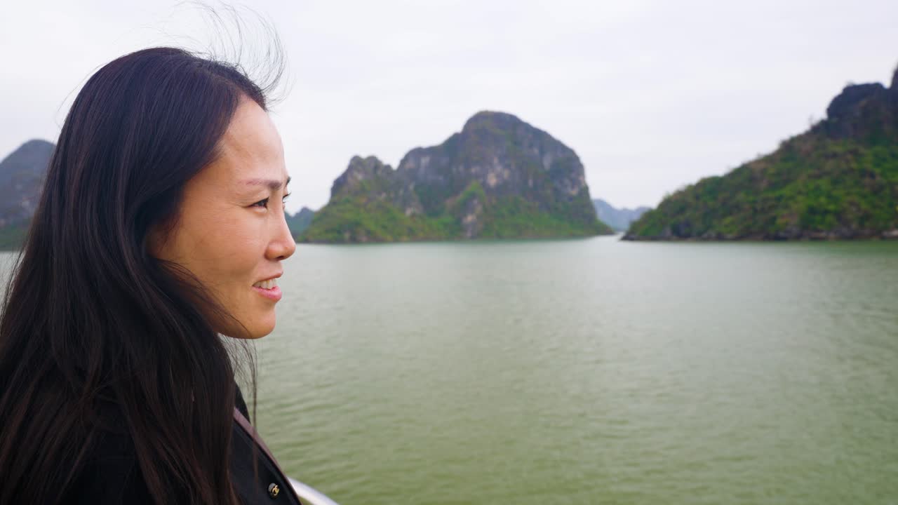 Happy Face close-up of Korean Woman at Cruise Ship Bow gazing contemplatively at limestone karsts and emerald waters of Ha Long Bay, Vietnam