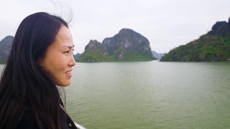 happy face close-up of korean woman at cruise ship bow gazing contemplatively at limestone karsts and emerald waters of ha long bay, vietnam