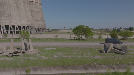 Aerial-tracking-shot-of-a-van-traveling-past-a-power-plant-chimney