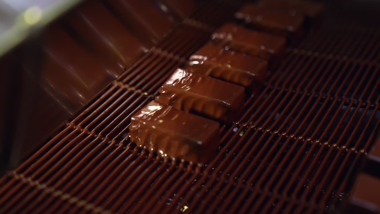 Sweets coming out of chocolate pouring and being blown by the air to make ripples. Delicious chocolate candies production. Close up.