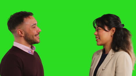 close up studio portrait of smiling male and female teachers or businesspeople talking before looking at camera against green screen