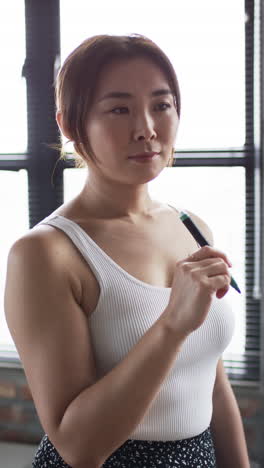 vertical video: businesswoman holding pen, thinking and planning in modern office setting