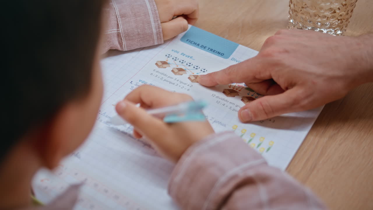 Schoolboy hand writing homework with teacher at table closeup. Child educating