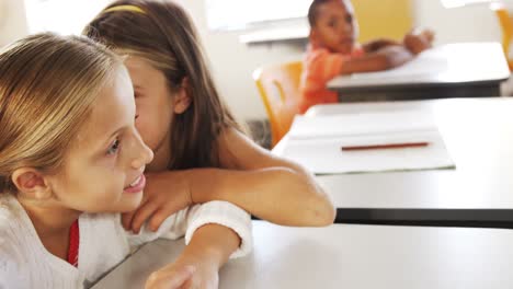 schoolgirl whispering into her friends ear in classroom