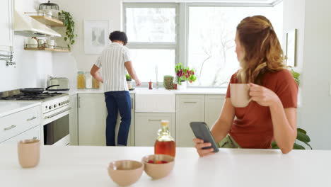 young woman preparing drinks in kitchen while man cooking in background, at home