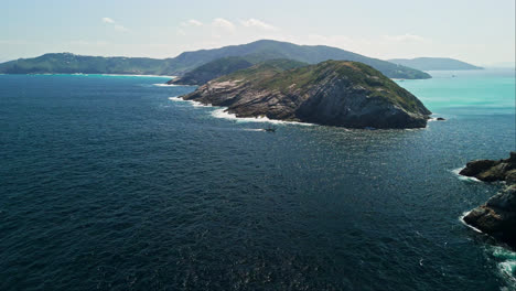 aerial dolly of a small island off the coast of brazil with clear blue waters and rocky shores, dazzling deep ocean with sloping grass along edge of rocks