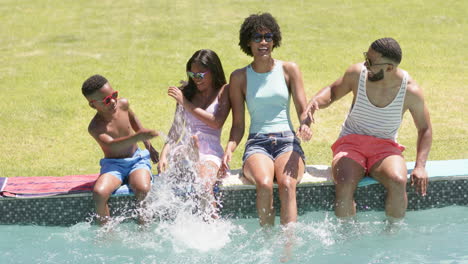 happy african american parents, son and daughter sitting in sun splashing, feet in pool, slow motion