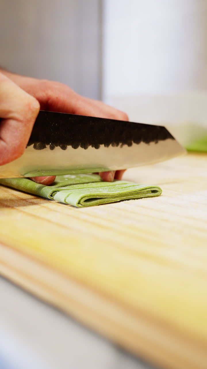 Mani che tagliano pasta fresca verde su un tagliere di legno