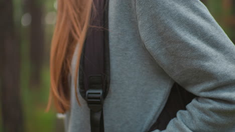 close-up of young woman in gray sweater, outdoors, with vibrant red hair and soft natural light in forest setting, focused on shoulder area