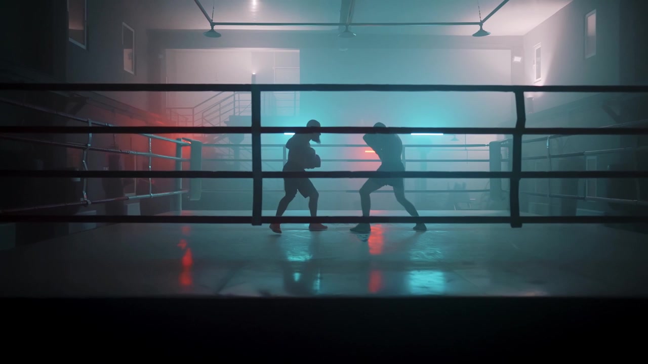 Sagome di due pugili che si allenano in un ring da boxe scuro con luci al neon