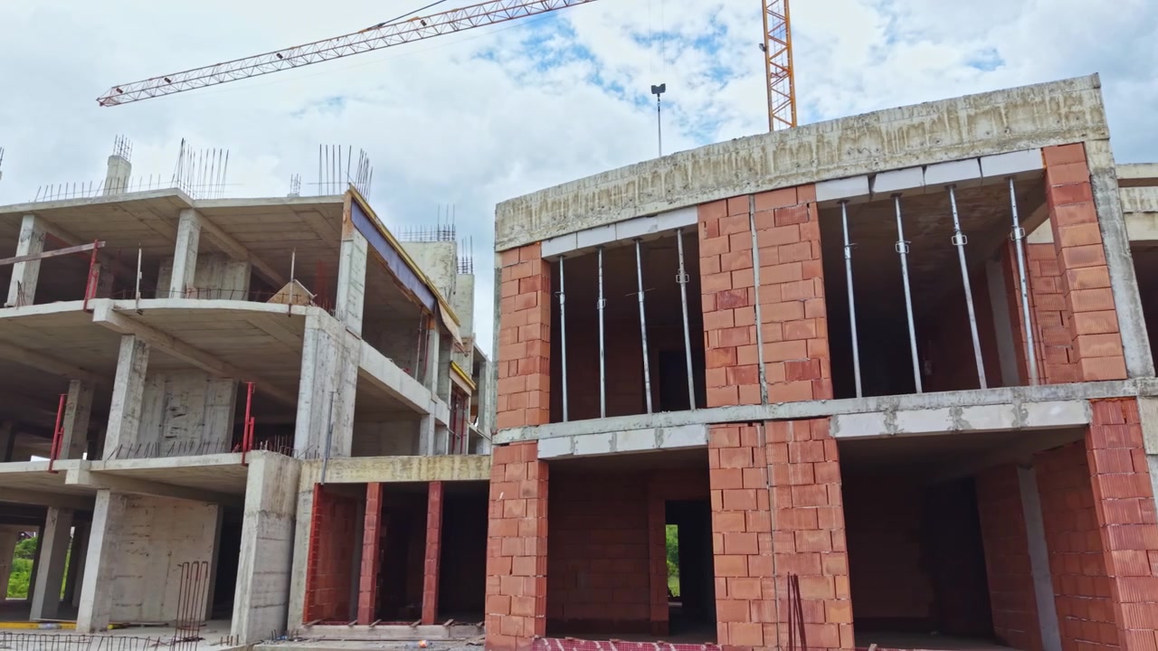 Trabajadores de la construcción edifican una nueva estructura en una obra en la ciudad durante el día con grúas operando y cielo nublado.