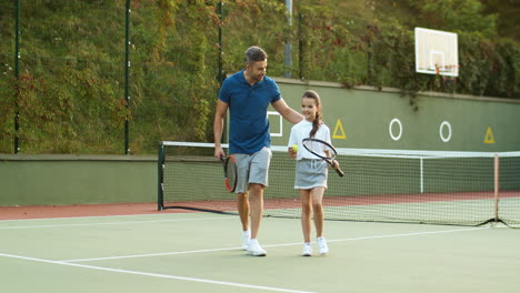 Liebevoller-Vater-Und-Glückliche-Kleine-Tochter,-Die-Scherzen-Und-Gemeinsam-Den-Tennisplatz-Verlassen