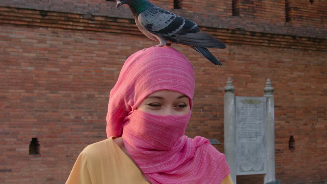Woman in Pink Hijab with Pigeon on Head at a Temple