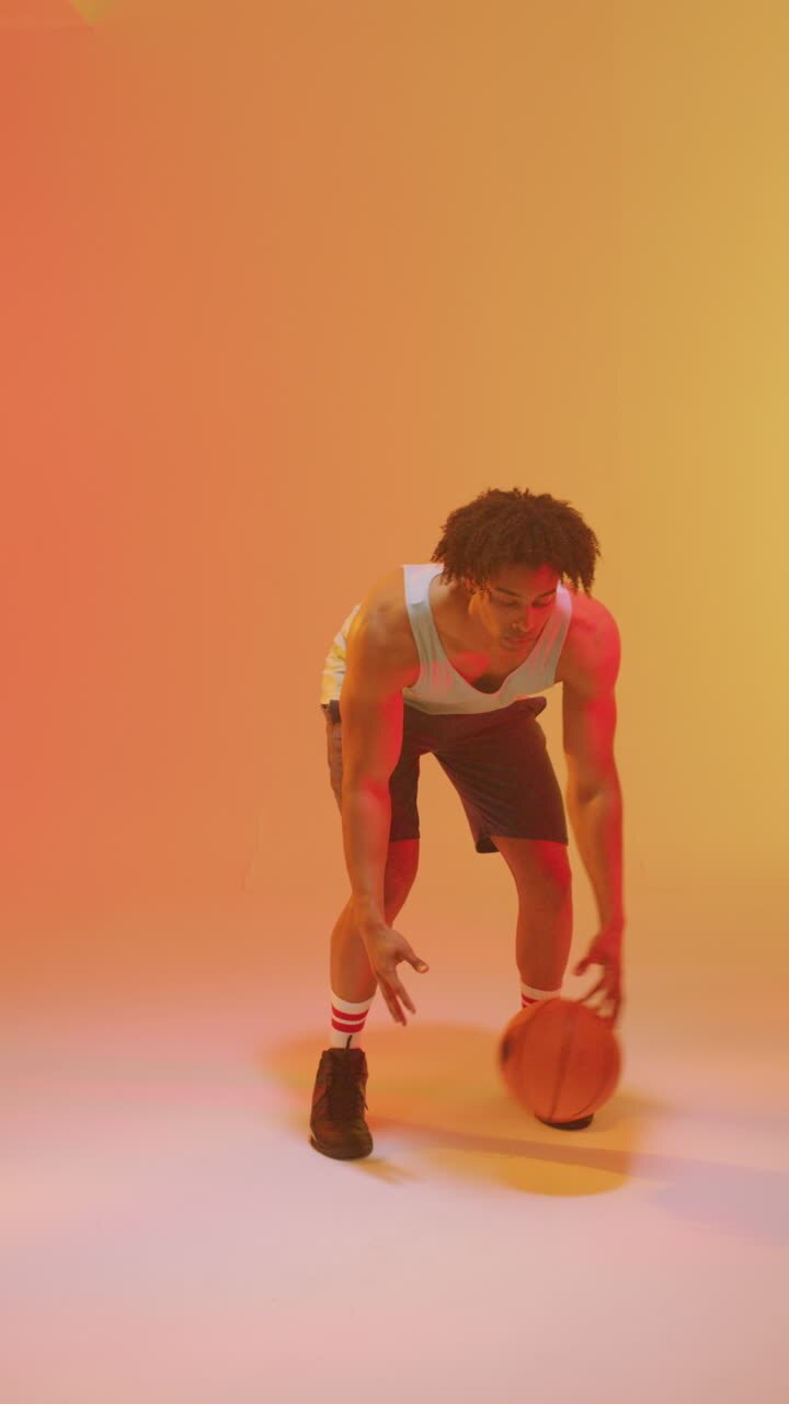 Vertikales Video eines männlichen Basketballspielers gemischter Herkunft mit Ball auf orangefarbenem Hintergrund