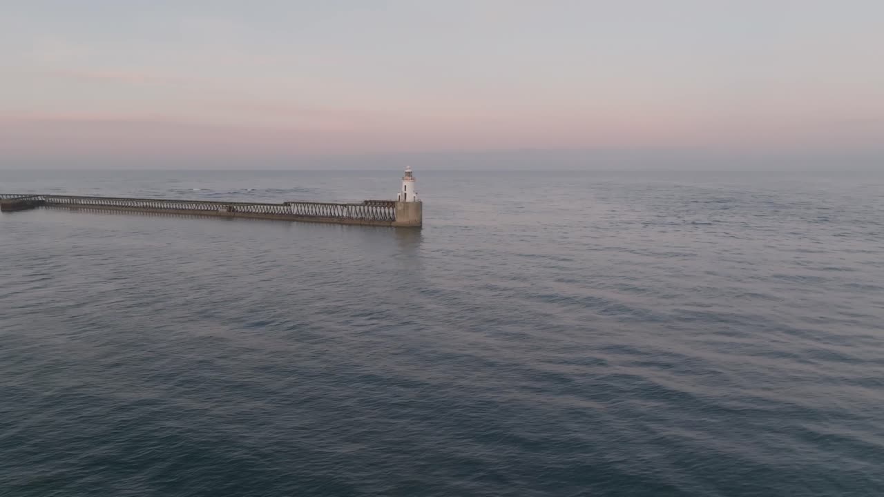 Sunset drone clip of lighthouse and harbour in Northumberland, England