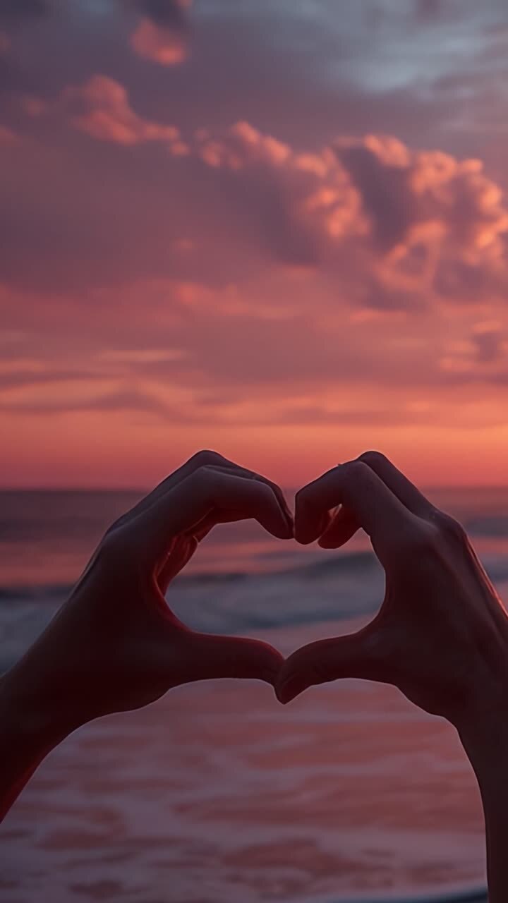 Un atardecer romántico en la playa: Dos manos formando un corazón contra un hermoso cielo crepuscular, iluminando el amor y la conexión en la orilla