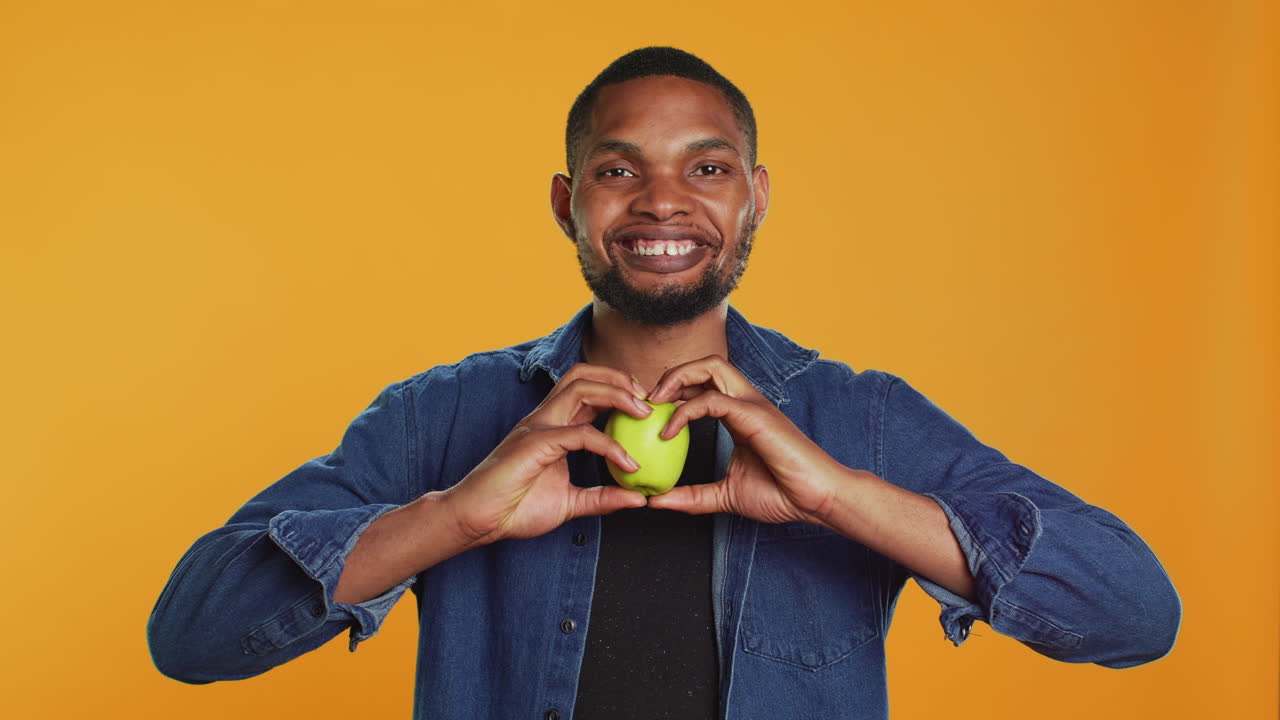 afroamericano relajado hace un signo en forma de corazón con una manzana