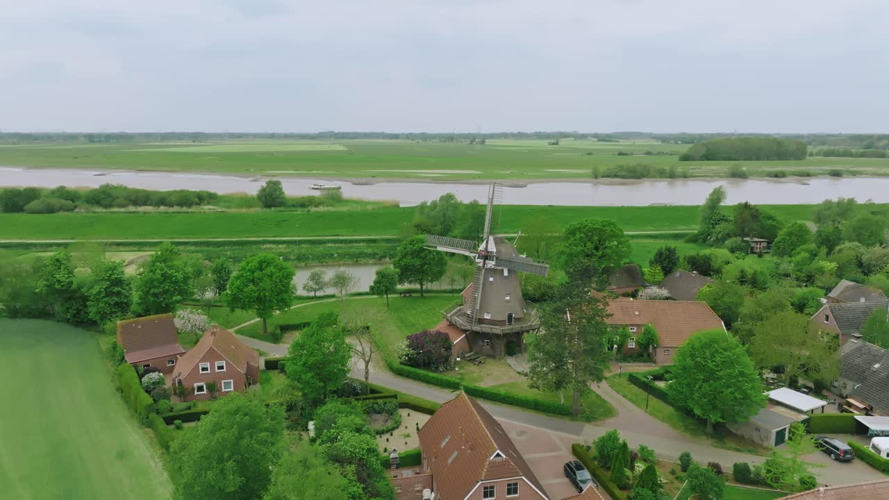 Drone performs a smooth semi orbit around a windmill at the heart of a rural German village. Diffused daylight with light cloud cover.