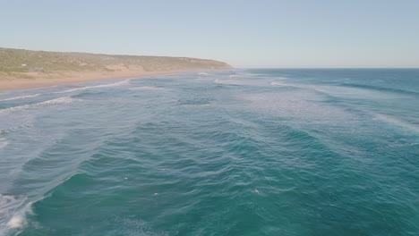 Aerial-shot-over-beach-as-waves-crash-into-shore-and-seagulls-fly-below