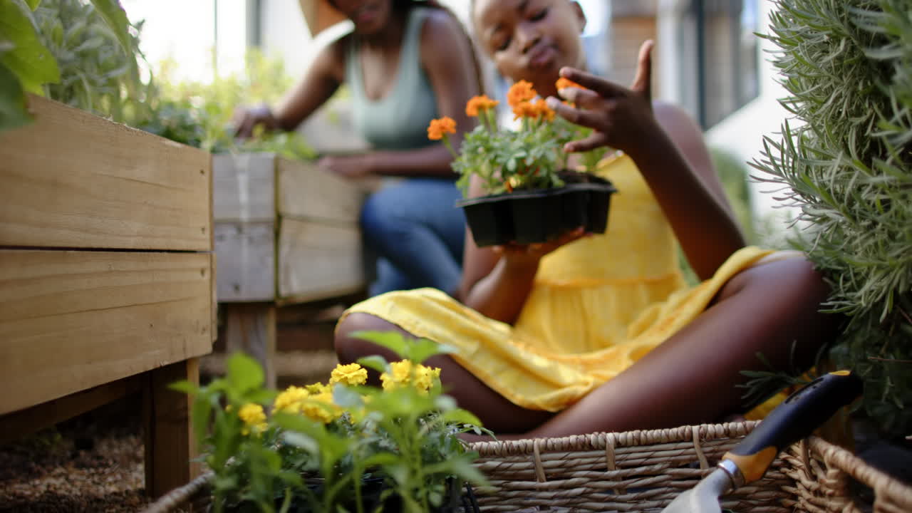 Gardening together, daughter holding flowers while mother planting in backyard garden