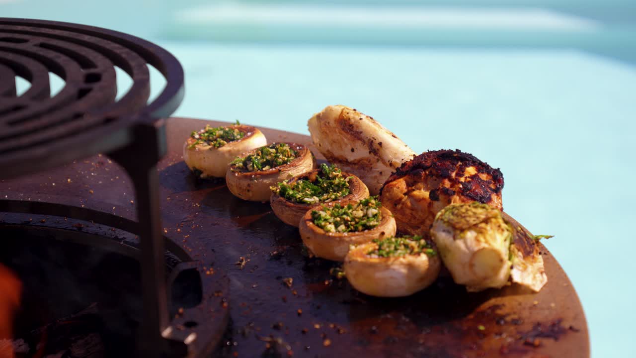 Pollo alla griglia e funghi ripieni cotti su una piastra rovente con fuoco, spezie ed erbe aromatiche