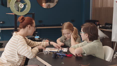 teacher and two teenagers constructing robot in workshop