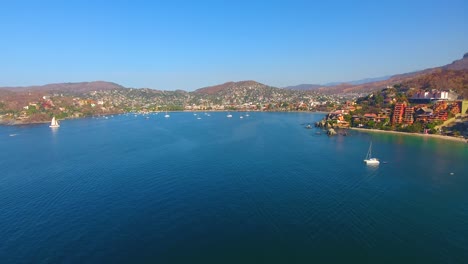 drone flying high above a still water bay with many boats anchored off the shore of a quiet town on the western coast of mexico