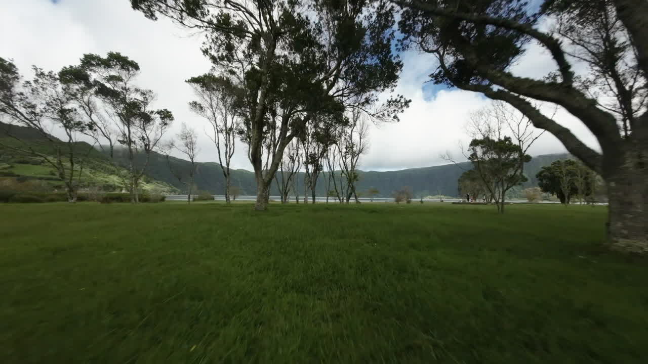 Low fast FPV aerial of trees, grass and woman by water at Azores