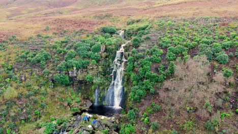 Yorkshire-Moors'-extraordinary-waterfall,-aerial-footage-captures-water-cascading-over-rocks-into-a-deep-blue-pool,-hikers-below