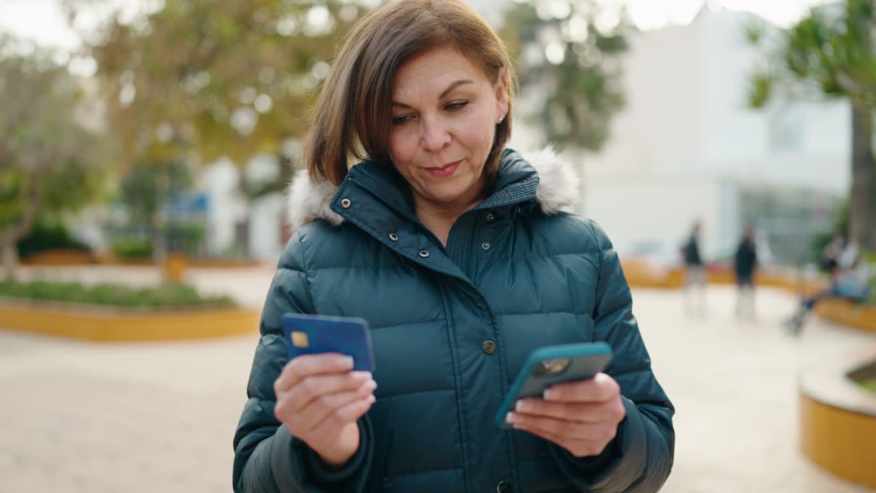 mujer de mediana edad usando teléfono inteligente y tarjeta de crédito en el parque
