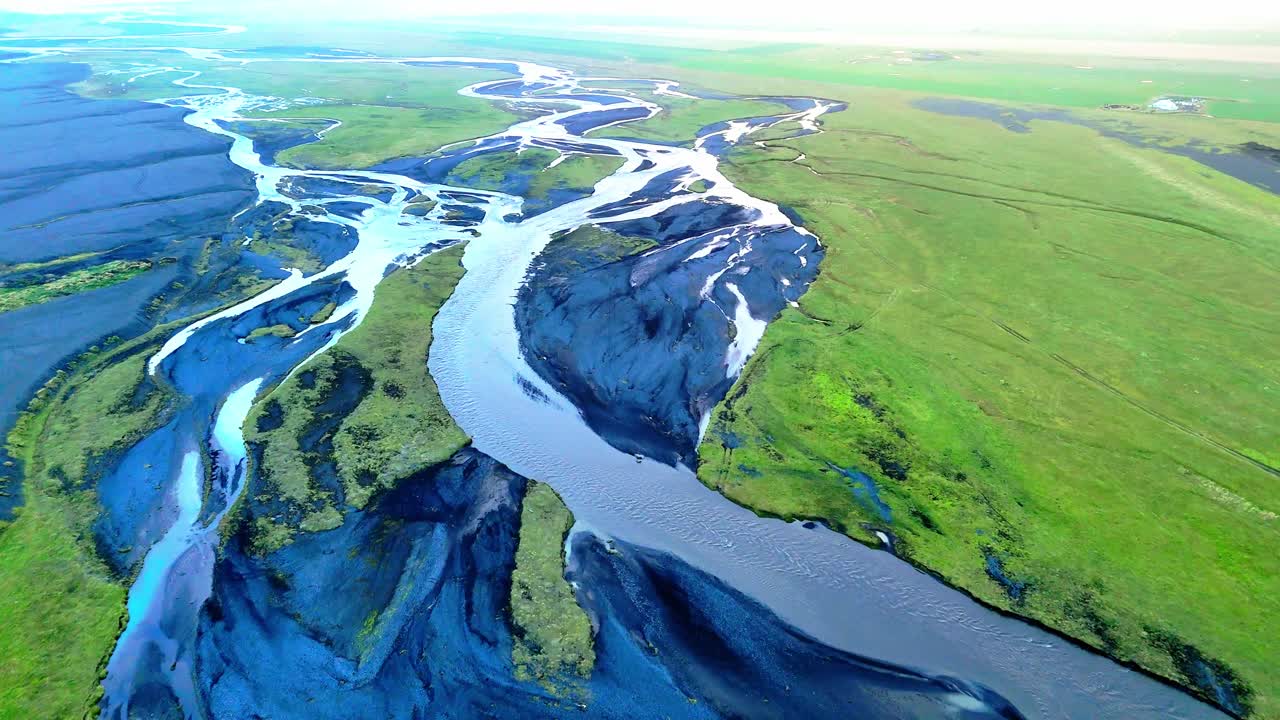 Icelandic streams twist like veins on their journet through glaciated valleys, volcanic rock and vibrant mossy green flatlands to the sea. Drone aerial reveal horizon