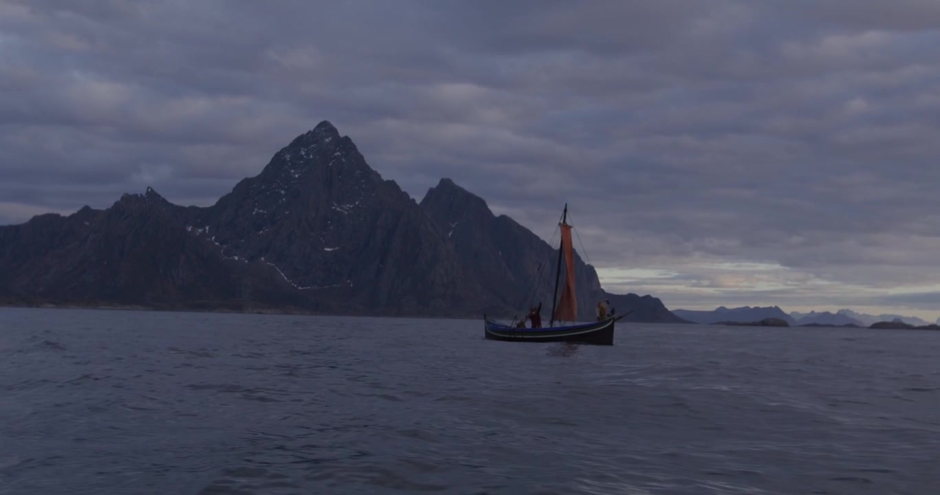 En lille båd med et rødbrunt sejl flyder på rolige fjordvande under en overskyet himmel, indrammet af mørke, majestætiske bjerge, hvilket fremkalder en fredfyldt og dramatisk stemning