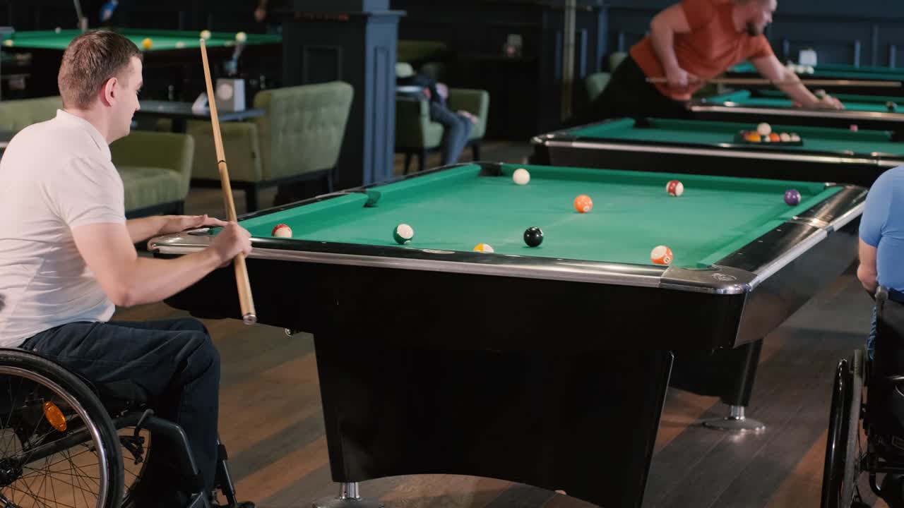 Adult men with disabilities in a wheelchair play billiards in the club